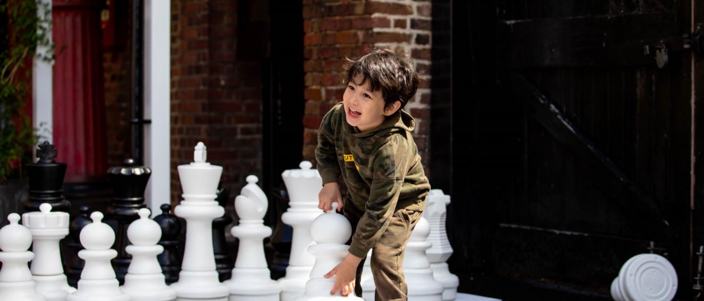 Boy playing with giant chess set outside Bruce Castle Museum