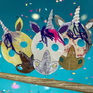 Three unicorn masks made by children above a narwhal horn.